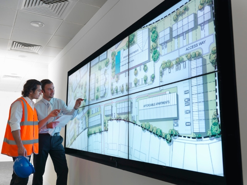 Two planners reviewing a large digital site plan, showing design and layout changes for rezoning applications in urban developments.