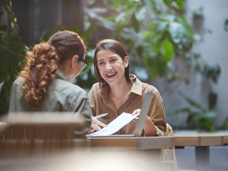 Two women discussing documents at a table with smiles, representing client consultation for what does a town planner do.