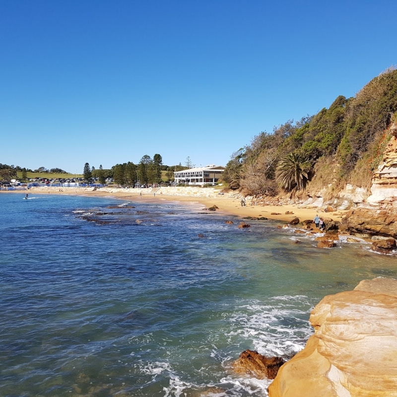 Coastal landscape for Town Planning Central Coast showing beach, rocky cliffs, vegetation, and nearby waterfront buildings.